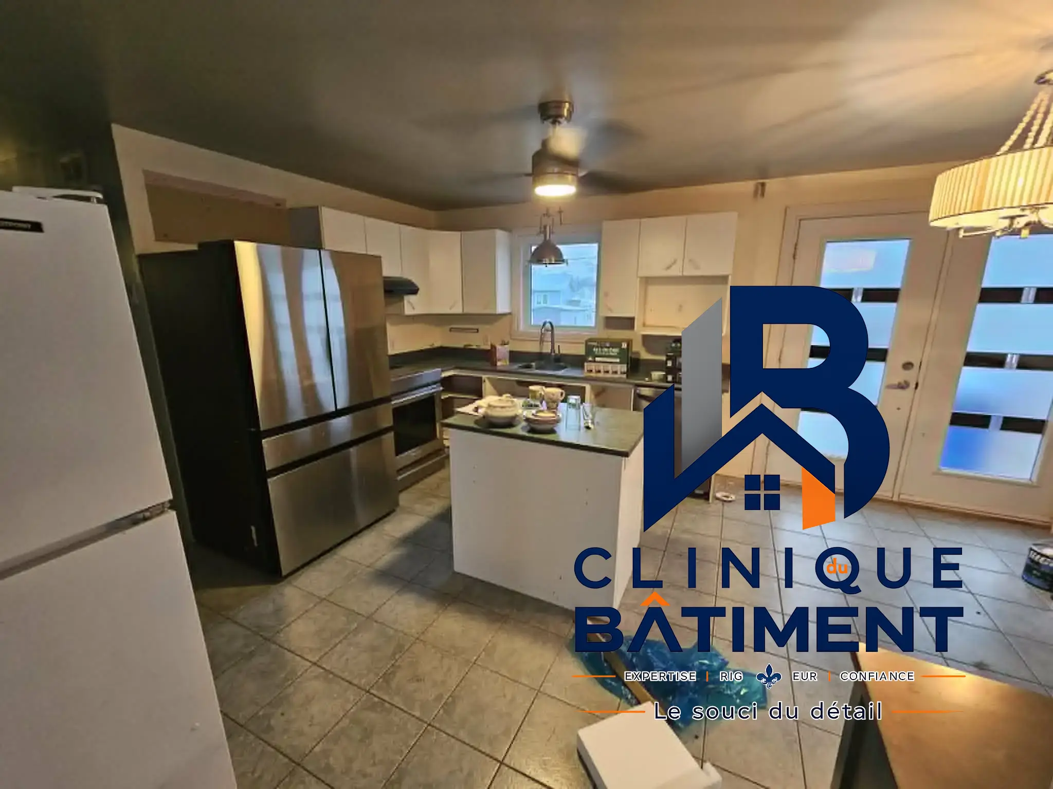Une cuisine équipée d'appareils en acier inoxydable, d'un îlot central et d'armoires blanches, paraissant fonctionnelle. Réalisation de cuisine à Brossard — Clinique du Bâtiment (RBQ 5821-2606-01).