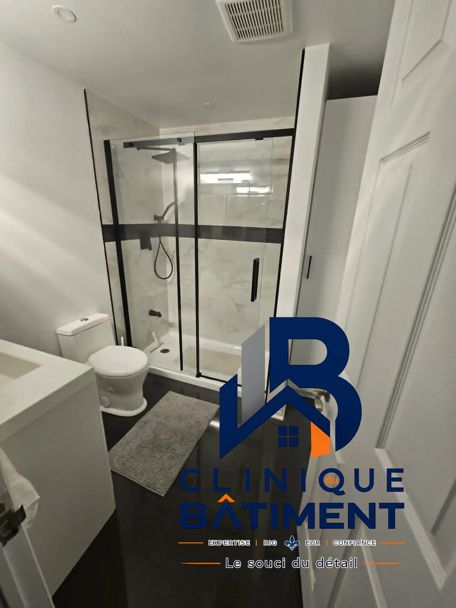 Une salle de bain moderne rénovée avec une douche vitrée, des toilettes blanches et un sol sombre. Réalisation de salle de bain à Brossard — Clinique du Bâtiment (RBQ 5821-2606-01).