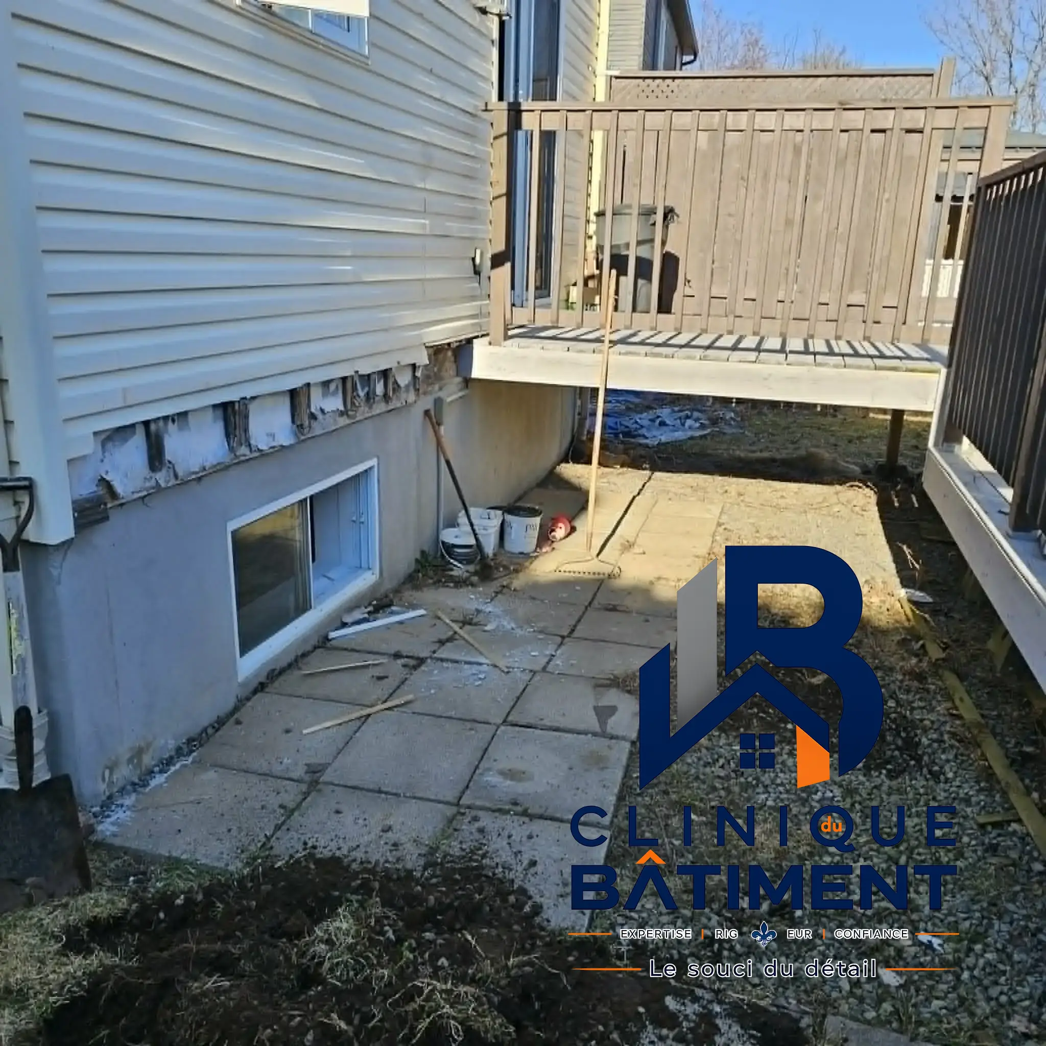 Vue extérieure d'une maison montrant le revêtement de façade partiellement retiré près de la fondation. Chantier de rénovation extérieure sur la Rive-Sud — Clinique du Bâtiment (RBQ 5821-2606-01).