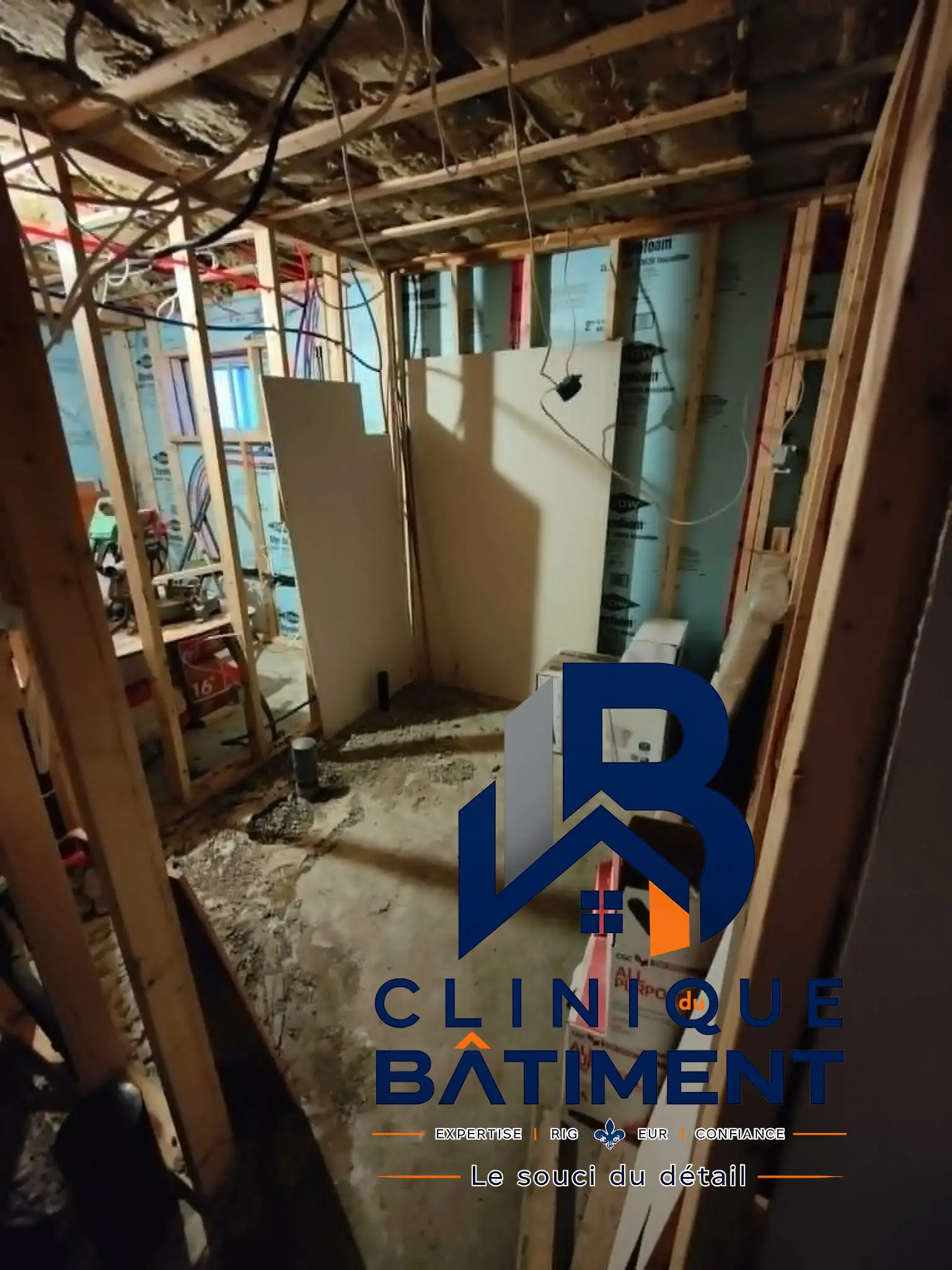 L'image montre une pièce en travaux avec l'ossature en bois exposée, des panneaux isolants et des câblages électriques en cours d'installation. Chantier de sous-sol à Boucherville — Clinique du Bâtiment (RBQ 5821-2606-01).